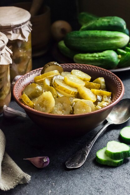 Pickled cucumber salad in a bowl and jars on black background