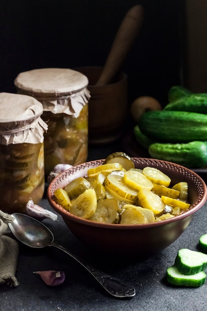 Pickled cucumber salad in a bowl and jars on black background