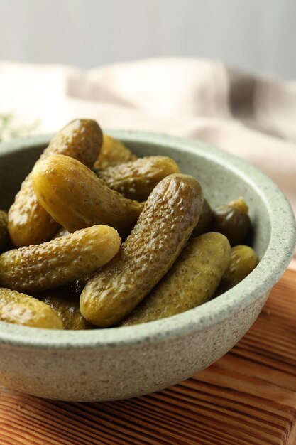 pickled cucumbers in bowl on wooden board closeup
