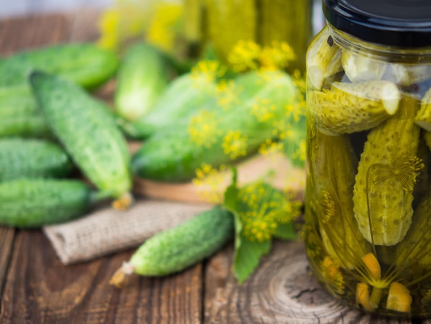 Pickled cucumbers in glass jars and fresh cucumbers and spices for making pickles on a wooden table