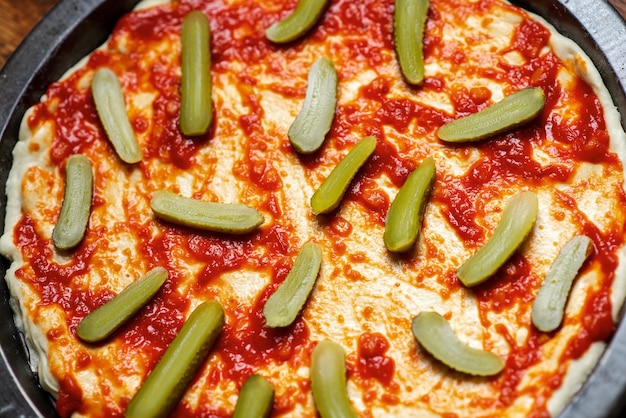 Pickled cucumbers laid out on a pizza crust covered with tomato sauce Cooking pizza with pickled cucumbers