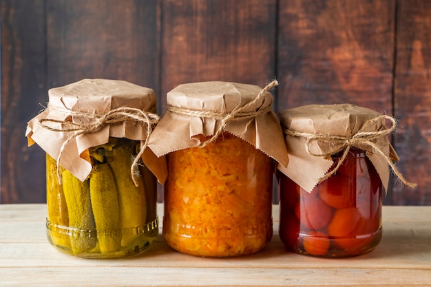 pickled farm vegetables in glass jars on a wooden background.