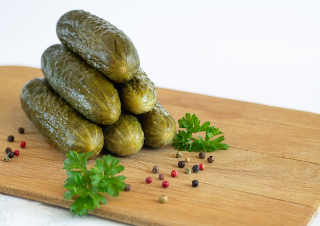 Pickled or fermented organic cucumbers with parsley and spice on wood board isolated on white background