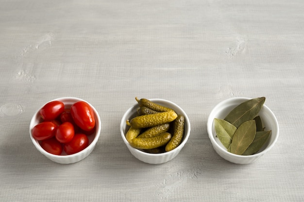 Pickled, fermented tomatoes and cucumbers and bay leaves in white bowls top view on a light wooden background with place for text