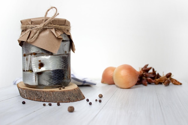 Pickled herring fish with pepper in jar on the table on light background