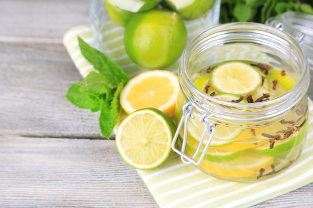 Pickled limes and cloves in glass jar on color wooden background