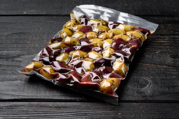 Pickled olives in vacuum sealed bag set on black wooden table\
background with copy space for text