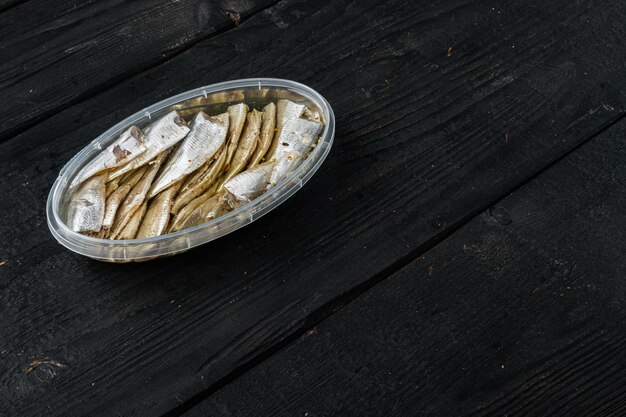 Pickled salted anchovies fillet set, in plastic container, on black wooden table