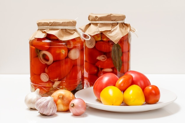 Pickled tomatoes in glass jars on white background.