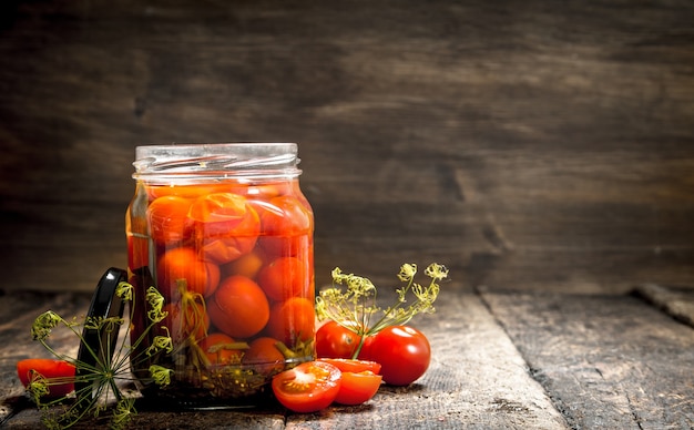 Pickled tomatoes with herbs and spices in jar.