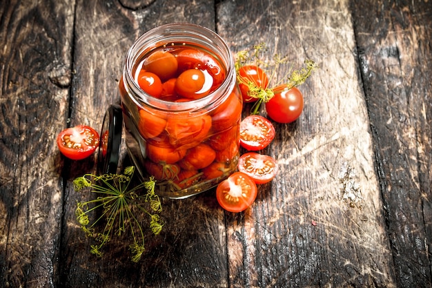 Pickled tomatoes with herbs and spices in jar.