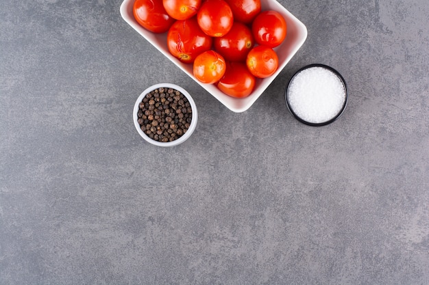 Pickled tomatoes with pepper corns placed on a stone table.