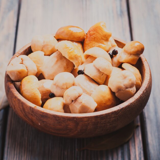 Pickled white boletus with black pepper and bay leaf in a wooden bowl