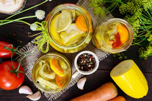 Pickles: vegetable assortment in glass jars on a dark wooden. The top view