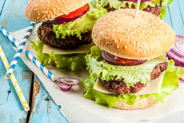 Picknick Fastfood Ongezond eten Heerlijke verse smakelijke hamburgers met rundvlees kotelet verse groenten en kaas op oude rustieke blauwe houten tafel met frisdrank water