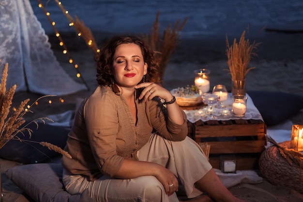 Picknick in de avond bij zonsondergang op de zandige kust van de zee of oceaan decor in boho en rustieke stijl portret van een mooie vrouw op een picknick