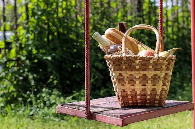 Picknick rieten mand met wijn, fruit en andere producten op een schommel met groene grasachtergrond