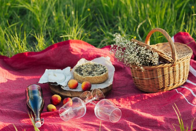 Picknick setting met lekkere cheesecake wijn kaas brie en mand met witte bloemen bij de natuur