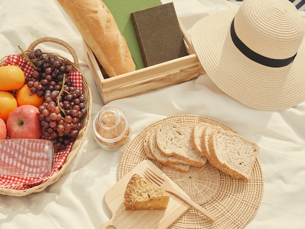 Picknickconcept Op de witte doek staan veel dingen zoals brood, fruit, een flesje water, een hoed en een notitieboekje.