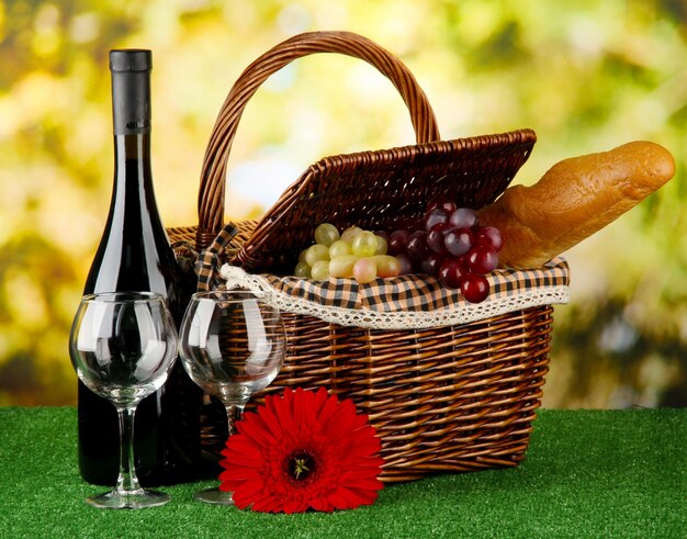 Picnic basket and bottle of wine on grass on bright background