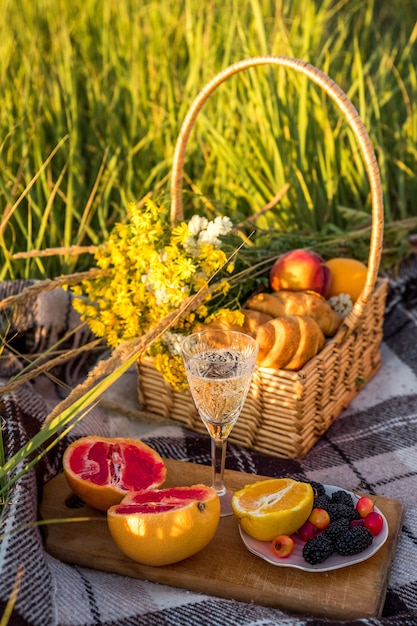 Корзина для пикника с едой и бокалом с шампанским на зеленой солнечной лужайке.