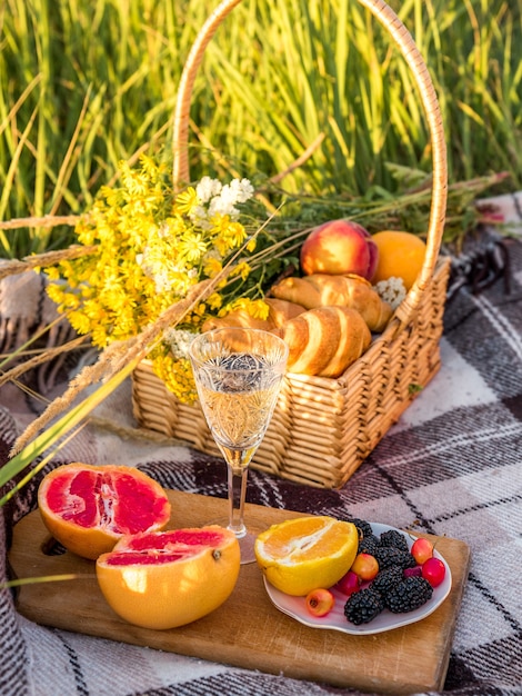 Picnic basket with food and glass with champagne on green sunny lawn.