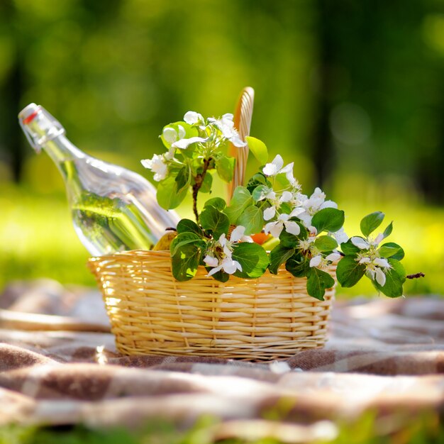 Picnic basket with fruits, flowers and water in the glass bottle 