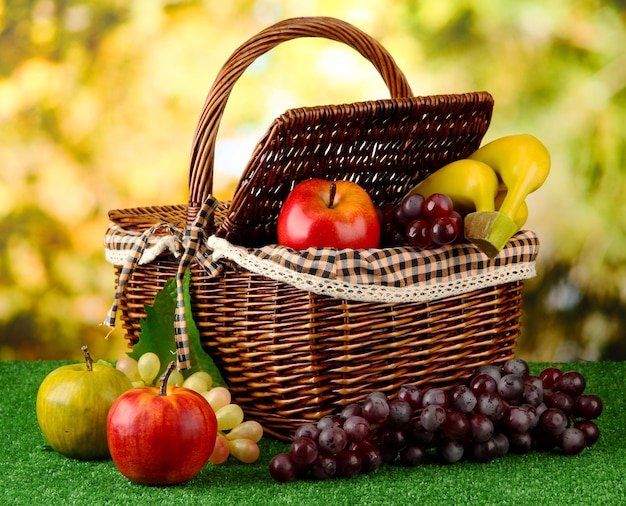 picnic basket with fruits on grass on bright background