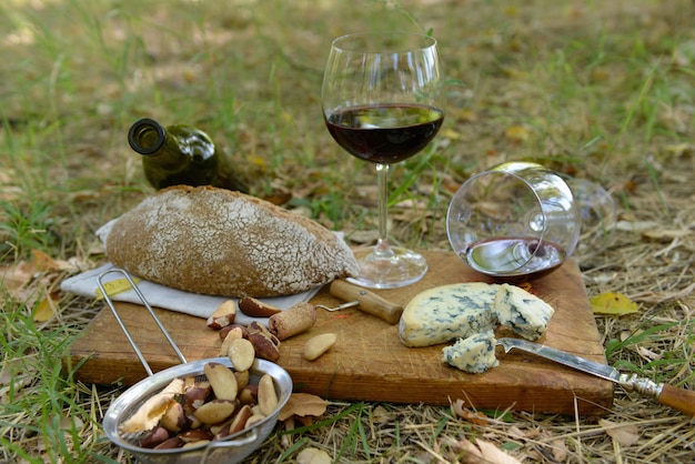 Picnic composition of red wine delicious cheese nuts and bread on wooden board outdoors