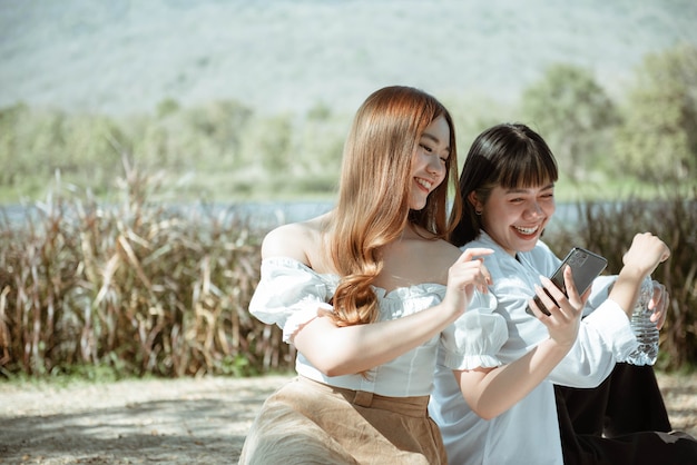 Picnic concept two smiling girls looking on the device screen checking photos they shot in a picnic moment.