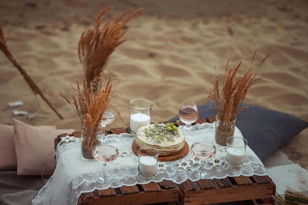 Пикник вечером на закате на песчаном берегу моря или океана в стиле бохо и деревенском стиле