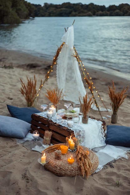 Picnic la sera al tramonto sulla riva sabbiosa del mare o dell'oceano con decorazioni in stile boho e rustico