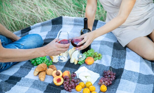 Foto picnic in natura, una ragazza e un uomo tengono in mano dei bicchieri con del vino. messa a fuoco selettiva