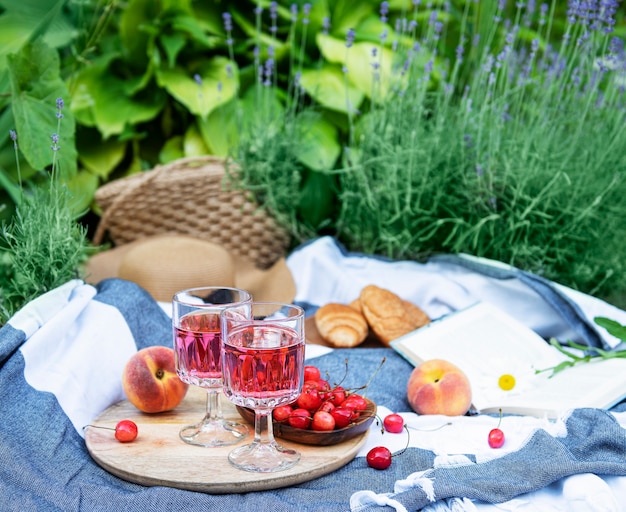 Picnic outdoors in lavender fields.  Rose wine in a glass, cherries  and straw hat on blanket