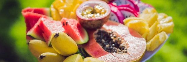 Foto picnic al parco sull'erba: un piatto di frutti tropicali sullo sfondo dell'erba banner, formato lungo