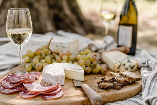 Photo picnic served outside with a bottle of wine cheese grapes salami on a wooden board