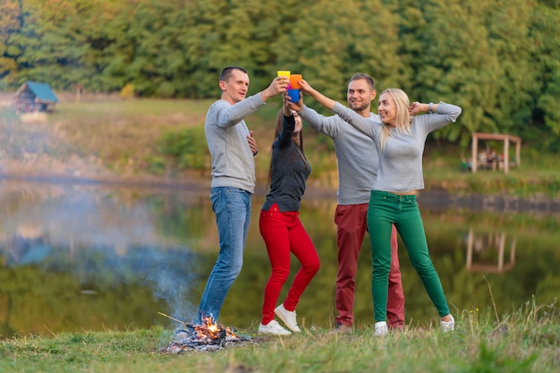 Picnic with friends in at lake near bonfire. Company friends having hike picnic nature background. Hikers relaxing during drink time. Summer picnic. Fun time with friends