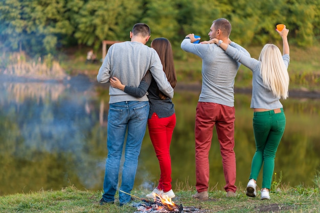 Fai un picnic con gli amici nel lago vicino al falò. amici della società che hanno escursione sul fondo della natura di picnic. escursionisti che si rilassano durante il drink. picnic estivo. divertimento con gli amici