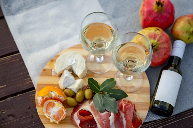 Photo picnic with wine prosciutto, cheese, olives, lies on a gray blanket, next to ripe pomegranates