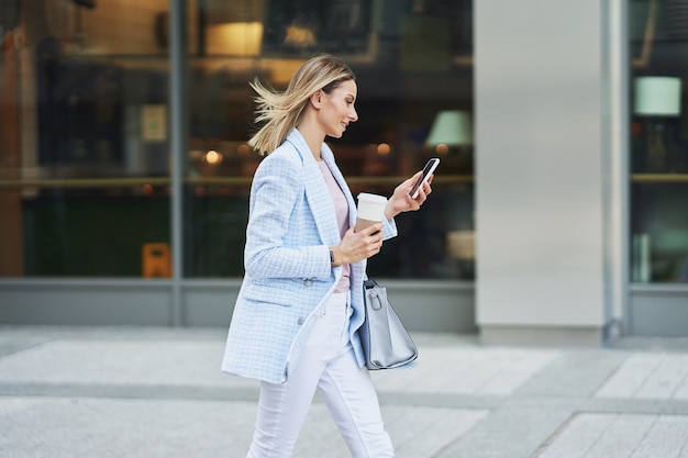 街を歩いているスマートフォンを持つ大人の魅力的な女性の写真