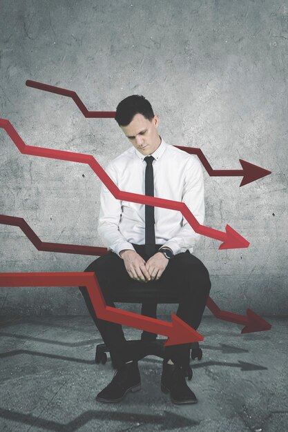 Photo picture of american businessman looks desperate while sitting on the chair with declining arrows