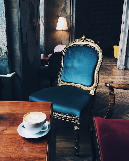 Immagine della sedia e della tazza antiche di cappuccino o di caffè espresso sulla tavola di legno nella stanza trascurata con le pareti infuriate