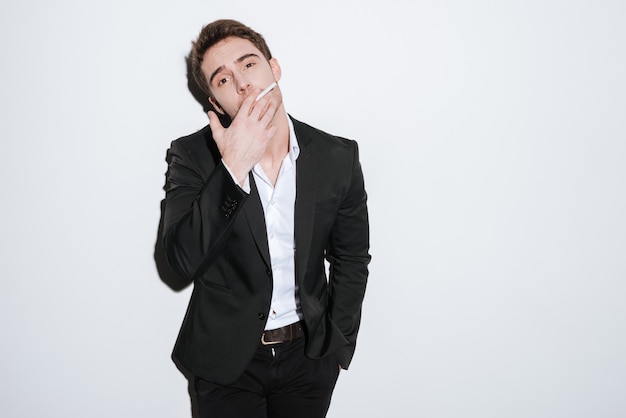 Picture of attractive businessman posing   while holding cigarette. Isolated over white wall.