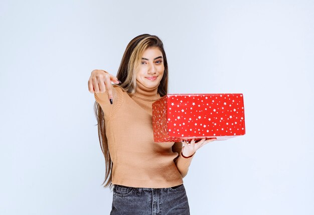 Picture of an attractive woman model holding a red present and pointing down.