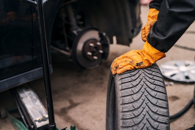 Picture of auto mechanics hands putting car tire on car in workshop.