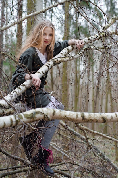 자작나무 가지에 앉아 있는 아름다운 금발 소녀의 사진
