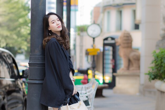 A picture of a beautiful long haired Asian lady in a black robe standing and looking out in the city