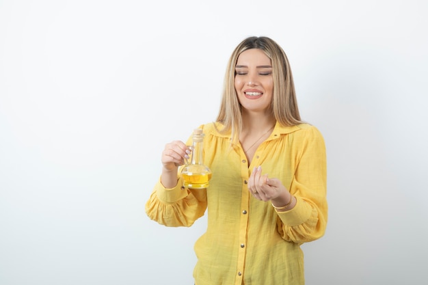 Picture of a beautiful woman model in yellow shirt holding a glass bottle of oil