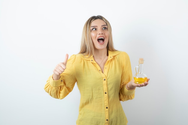 Picture of a beautiful woman showing thumb up and holding a glass bottle of oil