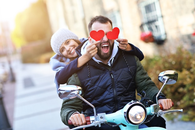 Picture of beautiful young couple smiling while riding scooter in city in autumn